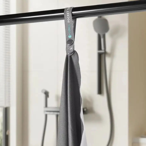 Gray towel hanging on a rack with text about a button loop for easy hanging, quick drying, ease of care, and machine washability.