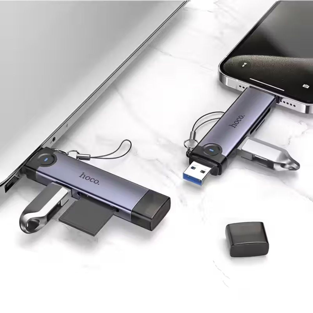 Two Hoco. USB flash drives in a metallic purple-gray finish are shown plugged into a laptop and smartphone on a white marble surface, with one drive's cap removed and placed beside it.