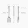 Joseph Joseph 3-piece stainless-steel BBQ turner, tongs, and fork set on a wooden surface, ready for grilling.