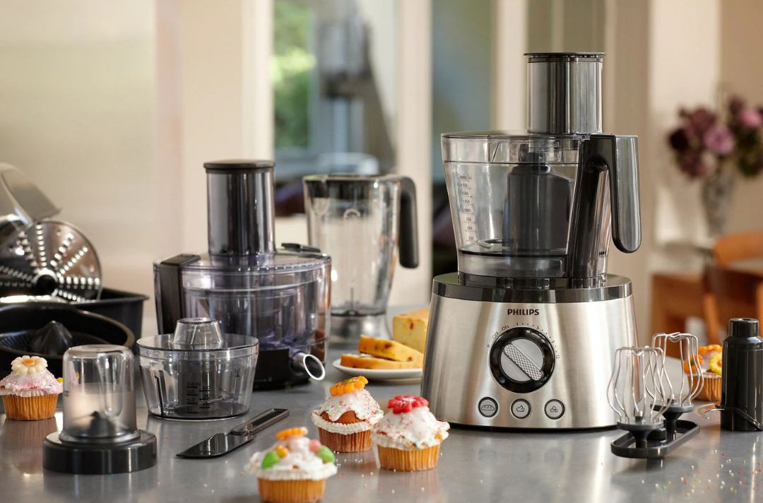 Kitchen appliances including a food processor and blenders on a counter with cupcakes.