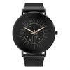 A round analog wristwatch with a black mesh strap, black case, and a black dial featuring a celestial sunburst design with gold-toned hands and small star details.
